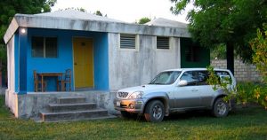 A white truck in front of a single story house in Haiti