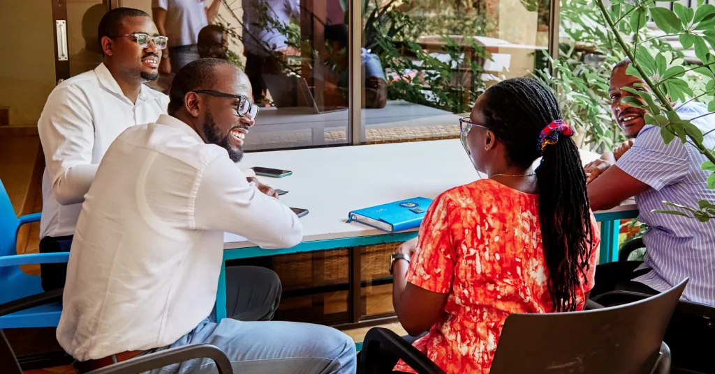 A group of staff discuss their project around a table in front of a glass wall