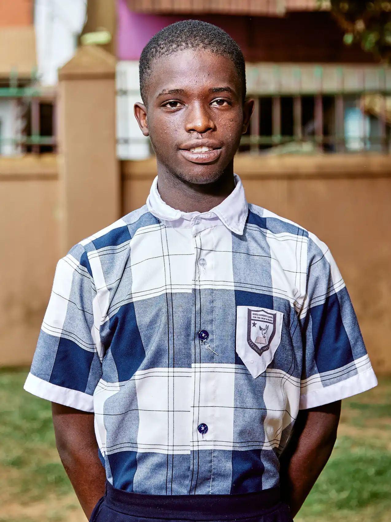 A young black man in a check school shirt standing outside a school for the dead and blind