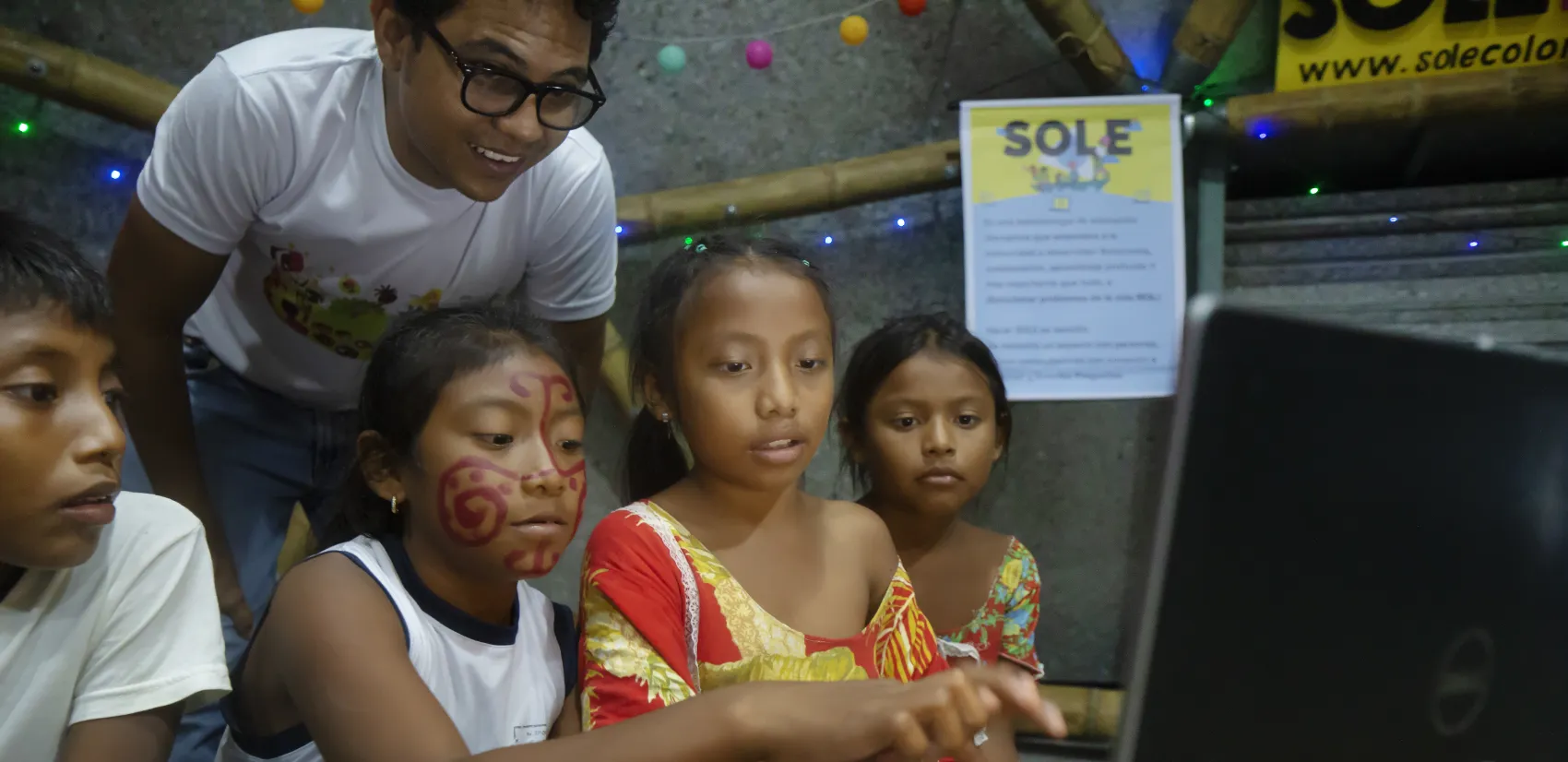 Three girls use a computer aided by a man