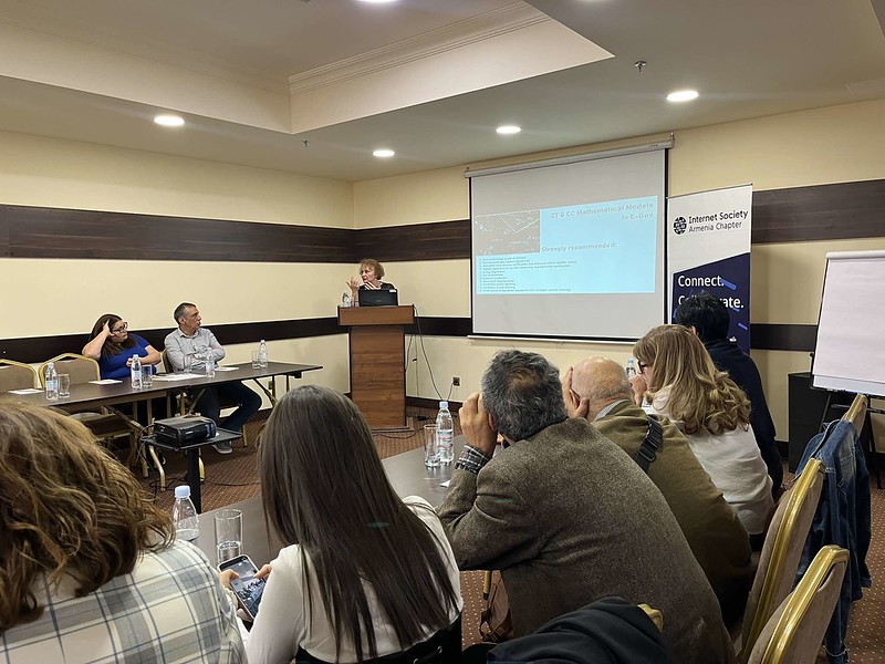 Participants listening to a female presenter in a conference room