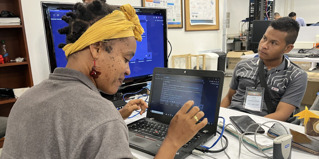 Young woman learning on a laptop with a male instructor watching her work