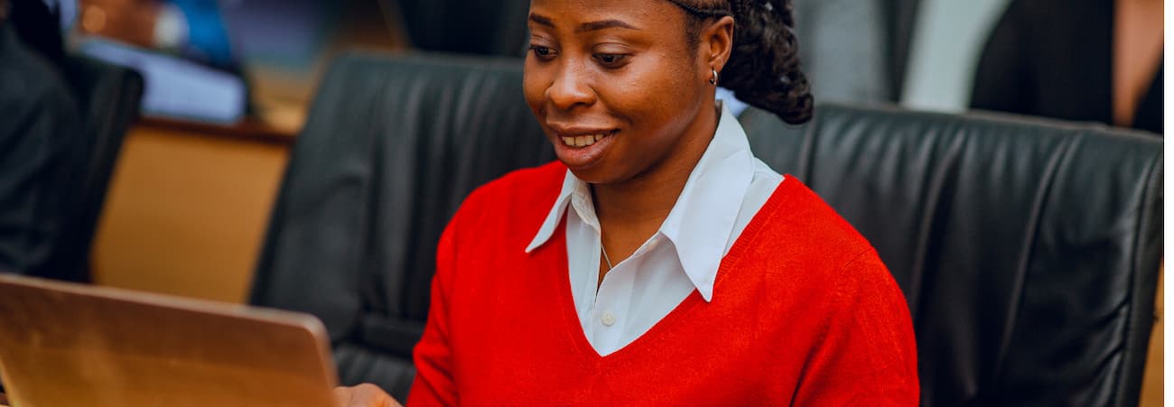 A woman in a red sweater gazes intently at her laptop screen.