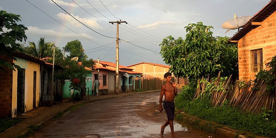 A man walks down a muddy street between houses